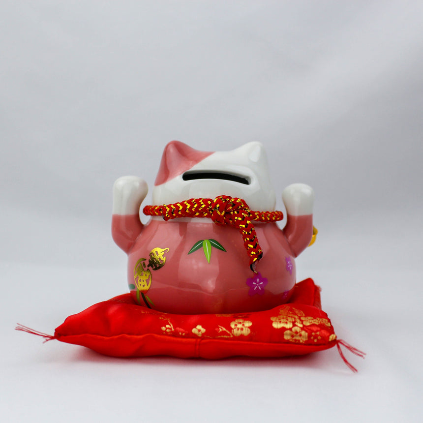 Ceramic Lucky Cat Coin Bank on Cushion, pink back view showing the coin slot and knotted red cord, seated on the cushion
