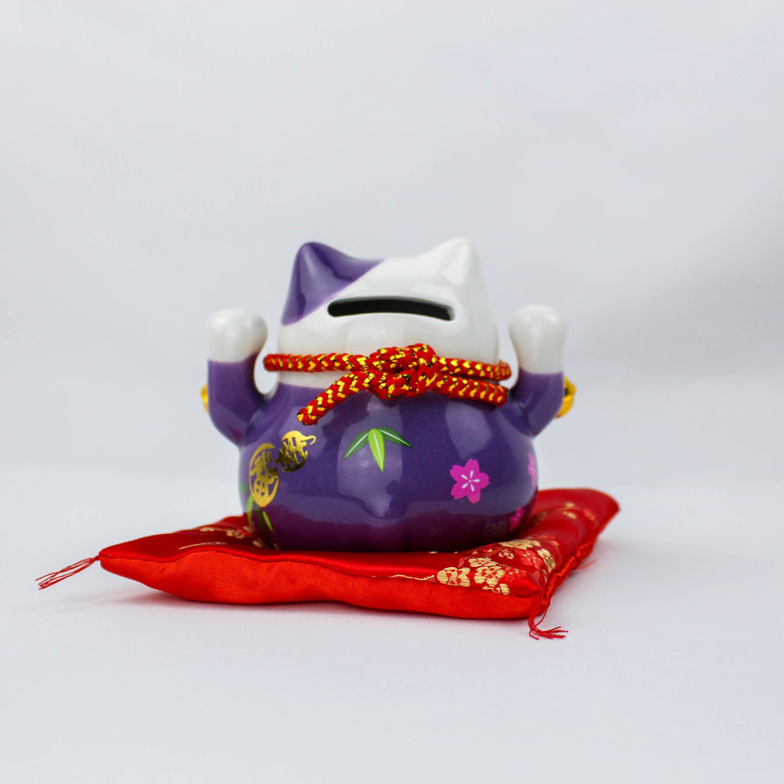 Ceramic Lucky Cat Coin Bank on Cushion, purple back view showing the coin slot and knotted red cord above painted bamboo